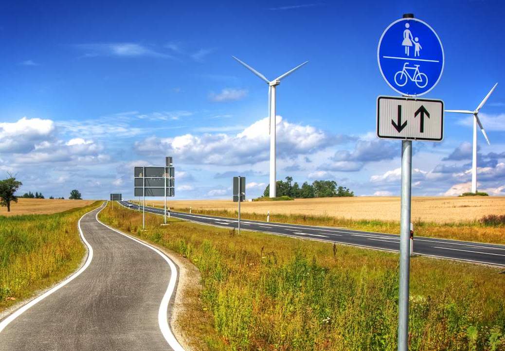 Radweg schlängelt sich durch Felder, Windräder am Horizont